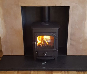 Clearview Pioneer 400 Multi-Fuel Stove - with flat top, 50mm legs in black installation with honed granite hearth and standard fascia rustic, light oak beam in Holmwood between Dorking and Horsham, West Sussex.